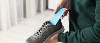 Person inserting a blue orthotic insole into a grey athletic shoe.