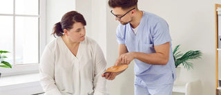 Healthcare professional showing an orthotic insole to a seated woman during a consultation.